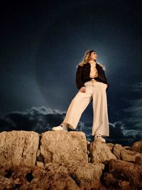 Woman sitting on rock by sea against sky