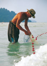 Full length of shirtless man standing at beach against sky