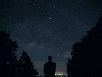 Rear view of silhouette man standing against sky at night