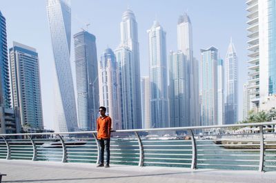 Young man standing by railing against buildings in city