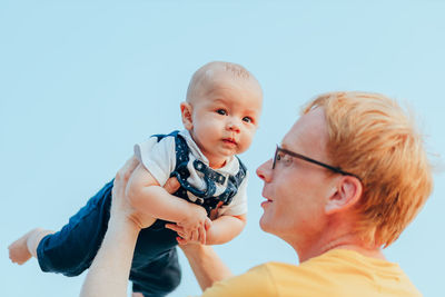 Father holding son mid-air against sky