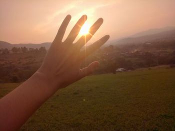 Close-up of hand on landscape against sky during sunset