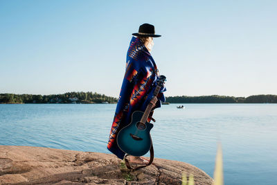 Woman wrapped in a pendleton blanket holding her guitar at the beach