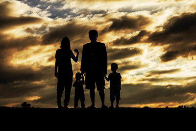 Silhouette family standing on field against orange clouds in sky