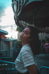 Side view portrait of young woman standing at amusement park during sunset