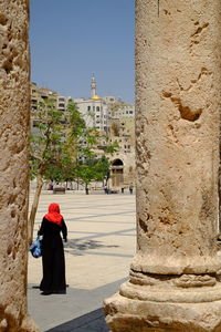 Rear view of woman walking by historic building against sky