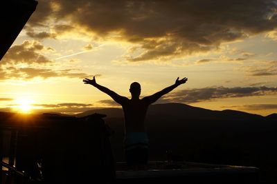 Silhouette man with arms outstretched standing against sky during sunset