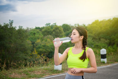 Young woman drinking water while standing on road