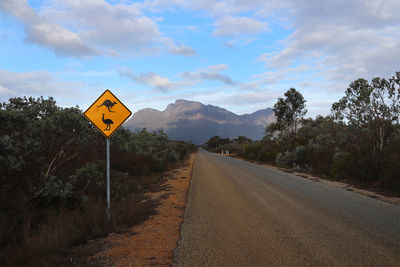 Road sign by trees against sky