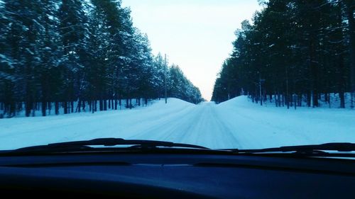 Road amidst trees seen through car windshield during winter