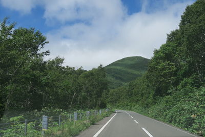 Country road amidst trees against sky