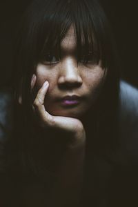 Close-up portrait of young woman with hand on chin against black background