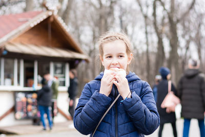 A cute girl takes a bite of a pie bought in a food truck in a city park in early spring