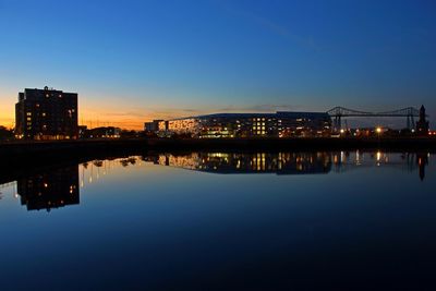 Illuminated buildings by river against sky at dusk