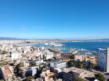 High angle view of townscape by sea against blue sky