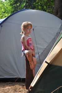 Portrait of girl sitting on wooden stump against tent