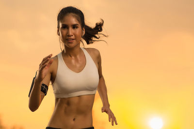 Smiling young woman jogging against orange sky during sunset