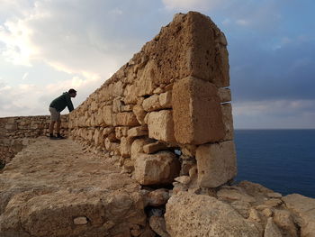 Man standing on rock by sea against sky