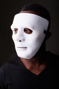 Close-up portrait of woman wearing mask against black background