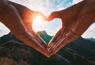Cropped hands of person making heart shape against mountains and sky