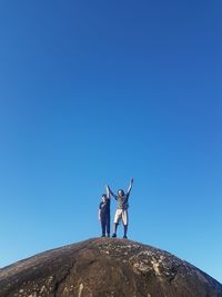 Low angle view of woman standing on rock against clear blue sky