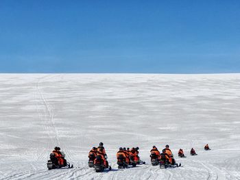 People on snow covered landscape against blue sky