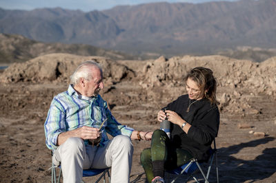 Woman and her grandfather talking while sitting on camping chairs outdoors in nature.