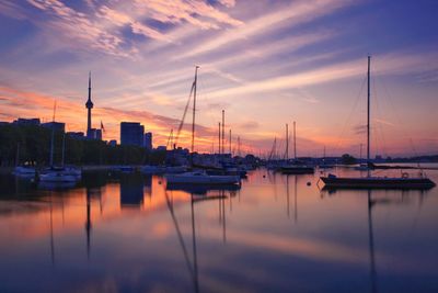 Boats moored in harbor at sunset