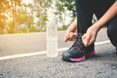 Low section of woman tying shoelace while kneeling by bottle on road