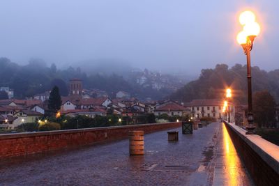 Illuminated street amidst buildings against sky at night