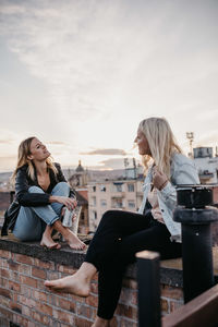 Woman sitting with umbrella against sky in city