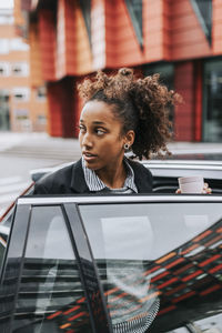 Young businesswoman looking away while embarking in car