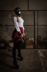 Woman with toxic protective mask holding axe in an underground warehouse