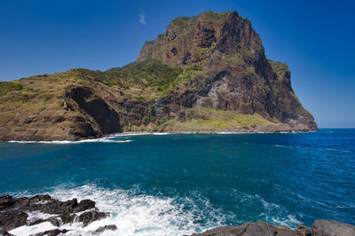 Scenic view of rocks by sea against blue sky