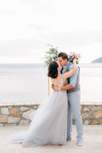 Couple holding umbrella while standing against sea