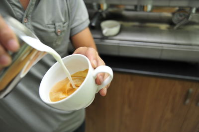 Midsection of woman pouring milk in coffee at cafe