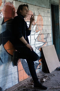 Side view of young woman standing against graffiti wall