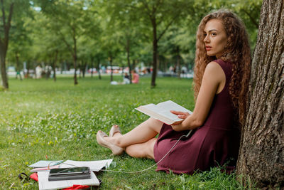 Portrait of young woman reading book while sitting on field