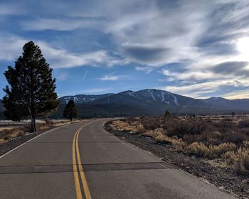 Empty road leading towards mountains against sky