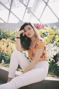 Portrait of young woman sitting by plants in park