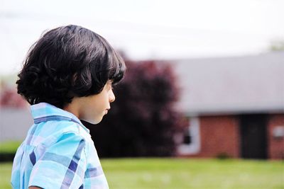 Side view of boy looking away while standing against sky at yard