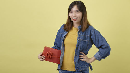 Portrait of smiling young woman against yellow background