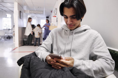 Young male patient waiting in outpatient clinic and using smart phone