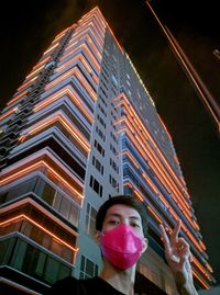 Low angle view of woman looking at illuminated building in city at night
