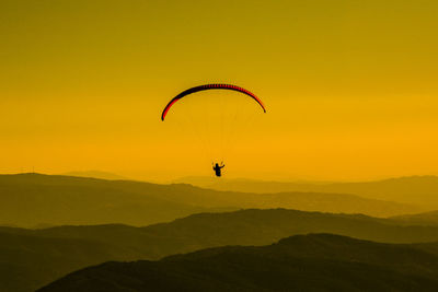 Silhouette person paragliding against sky during sunset