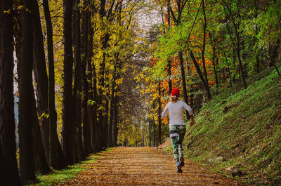 Rear view of woman running on pathway in forest during autumn