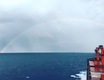 Container ship with rainbow over sea against sky