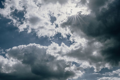 Low angle view of sunlight streaming through clouds