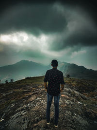 Rear view of man standing on mountain against sky