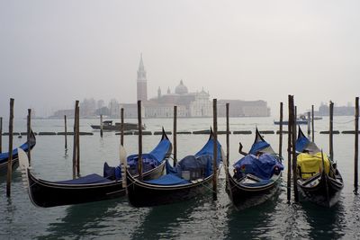 Gondolas moored in grand canal against san giorgio maggiore during foggy weather